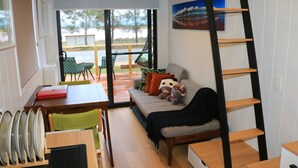 A cozy living area with a sofa, a dining table, and a ladder shelf. - The Pink Lake Tiny House - 'sakura' (Lochiel)
