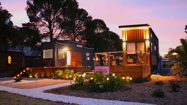 A modern house with a wooden exterior and a glass upper level, surrounded by a garden with a pathway and small plants. - The Pink Lake Tiny House - 'sakura' (Lochiel)
