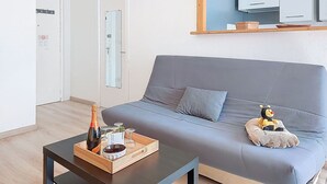 Un salon moderne avec un canapé gris, une table basse en bois sur laquelle se trouvent une bouteille et des verres, et un petit jouet en peluche.