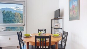 Un coin repas avec une table ronde, des chaises noires et une vue sur les montagnes par la fenêtre.