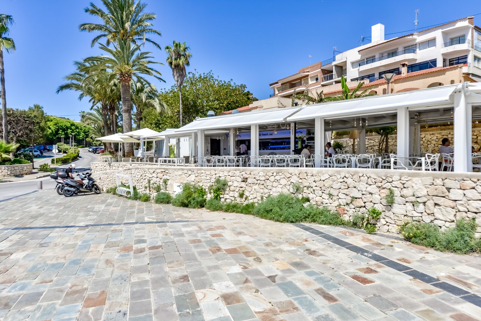 Un restaurant en bord de mer avec une terrasse, des murs en pierre et des palmiers.