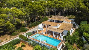 Uma grande villa com piscina, várias varandas e vegetação exuberante ao redor da propriedade.