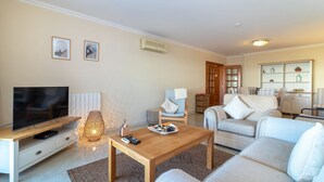 A modern living room with a flat-screen TV, a wooden coffee table, a sofa, a chair, and a decorative lamp. - Casa Bela Vista - Communal pool, close to town centre, beach and amenties (Carvoeiro)