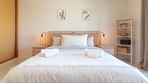 A hotel room with a large bed, two bedside tables with lamps, a wooden shelf with baskets, and two wall art pieces. - Casa Bela Vista - Communal pool, close to town centre, beach and amenties (Carvoeiro)