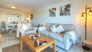 A living room with a sofa set, a coffee table, a dining area, and wall art. - Casa Bela Vista - Communal pool, close to town centre, beach and amenties (Carvoeiro)