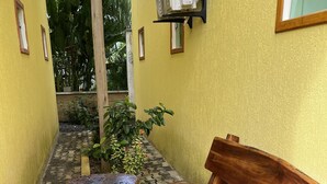A narrow outdoor corridor with a bench and wooden stools, a wall-mounted air conditioner, and potted plants. - POUSADA BRILHO DO MAR (Maraú)