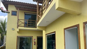 A two-story building with a yellow exterior, a balcony, and a glass door leading to a covered outdoor area. - POUSADA BRILHO DO MAR (Maraú)