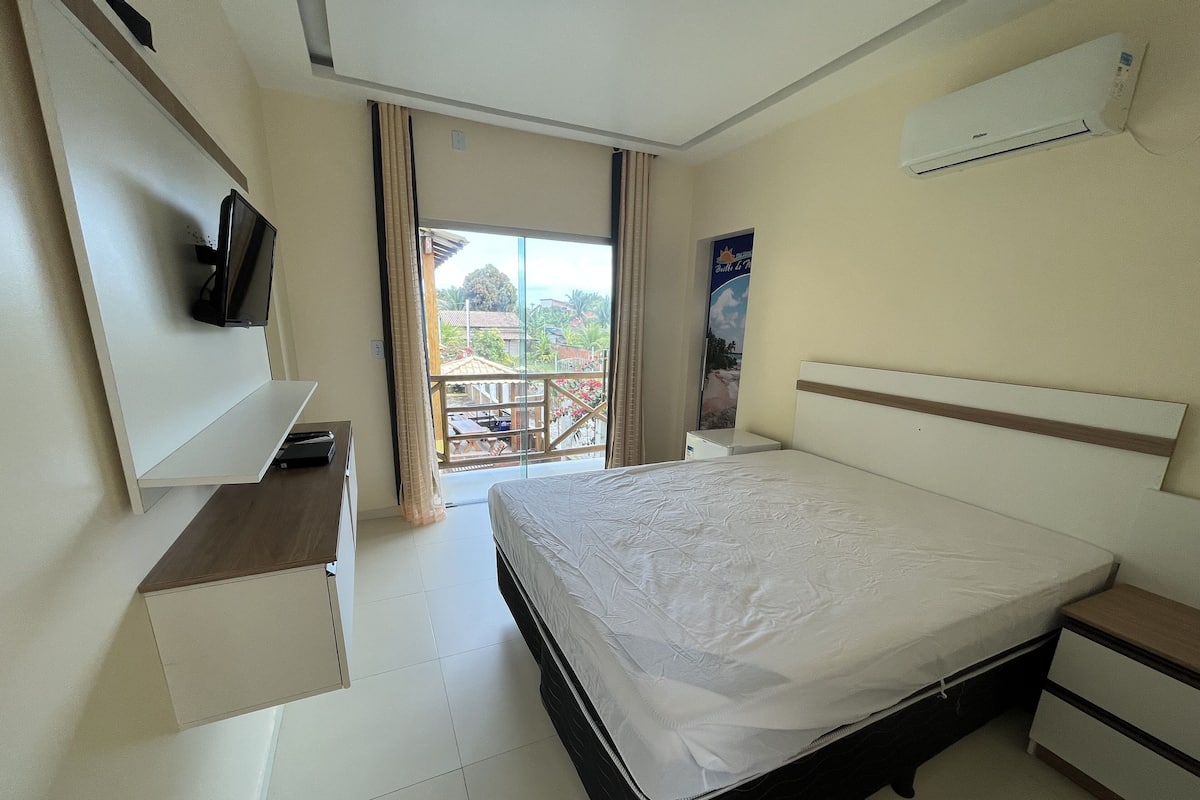 Habitación de hotel con cama, televisor montado en la pared, un escritorio pequeño y un balcón con vistas.