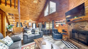 Interior acogedor de una cabaña con chimenea, paredes de madera, un comedor y una sala de estar con sofá y sillones.