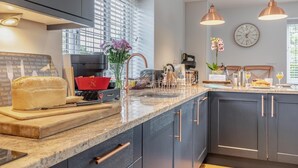 A modern kitchen with dark cabinetry, a marble countertop, a coffee machine, and pendant lighting.