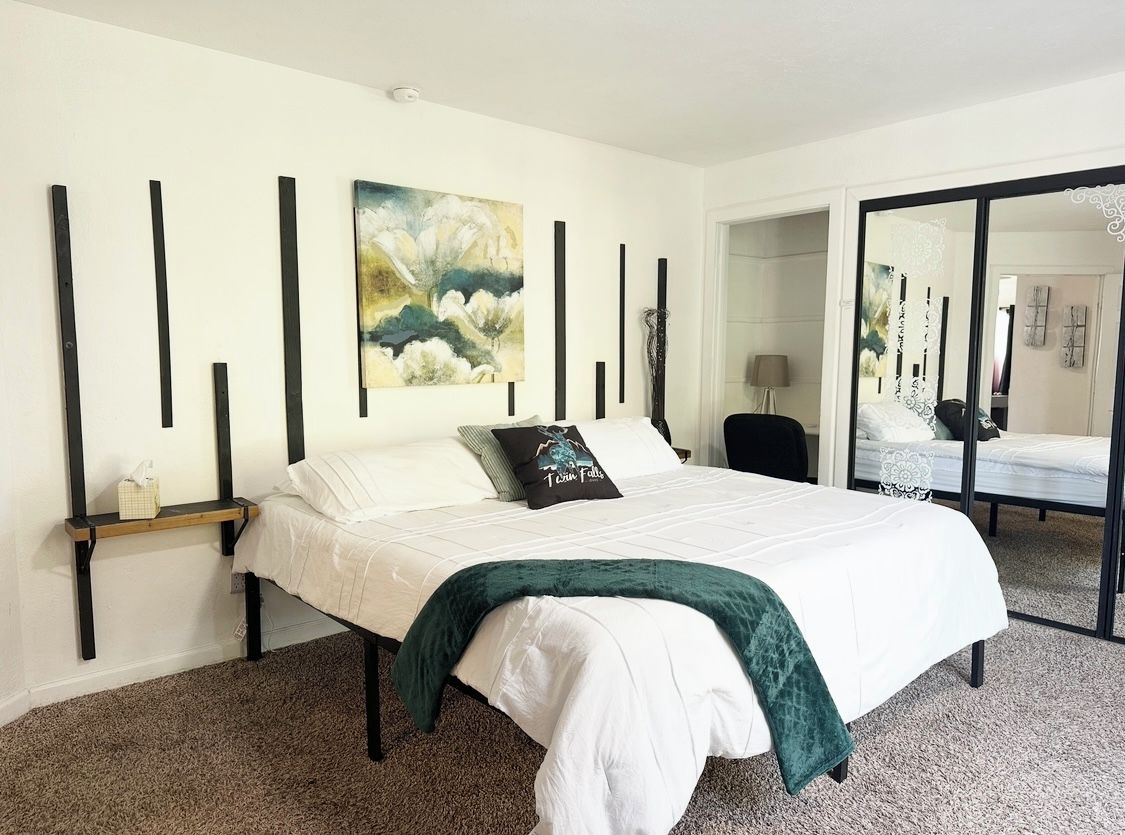 Quarto com cama, mesa de cabeceira, espelho e quadro na parede.