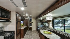 A compact RV kitchen with a stove, microwave, and a small dining area with a bench and a table. - ⛱ Heartland North Trail 31' RV (Manchaca)