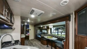 A compact RV kitchen with a sink, stove, and a dining area with a bench. - ⛱ Heartland North Trail 31' RV (Manchaca)