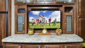 A kitchen with wooden cabinets, a marble countertop, a built-in TV, and a skylight. - ⛱ Heartland North Trail 31' RV (Manchaca)
