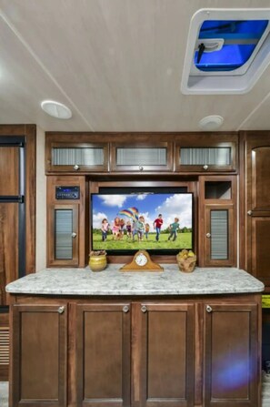 A kitchen with wooden cabinets, a marble countertop, a built-in TV, and a skylight. - ⛱ Heartland North Trail 31' RV (Manchaca)
