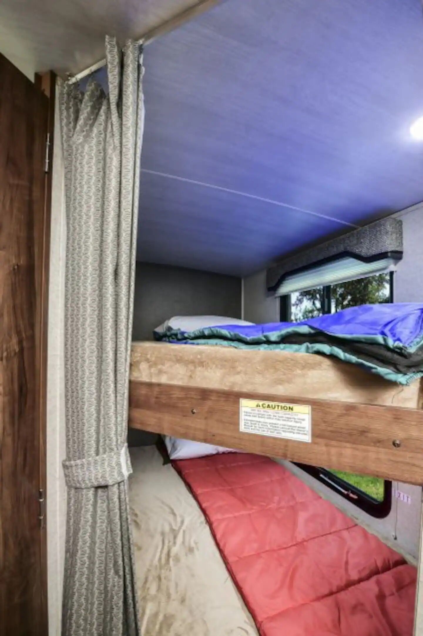 A bunk bed with a caution sign, a window with a view, and a curtain.