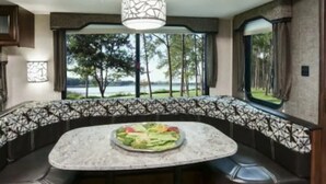 A cozy seating area with a round table, a bowl of fruit, and a view of the outdoors. - ⛱ Heartland North Trail 31' RV (Manchaca)