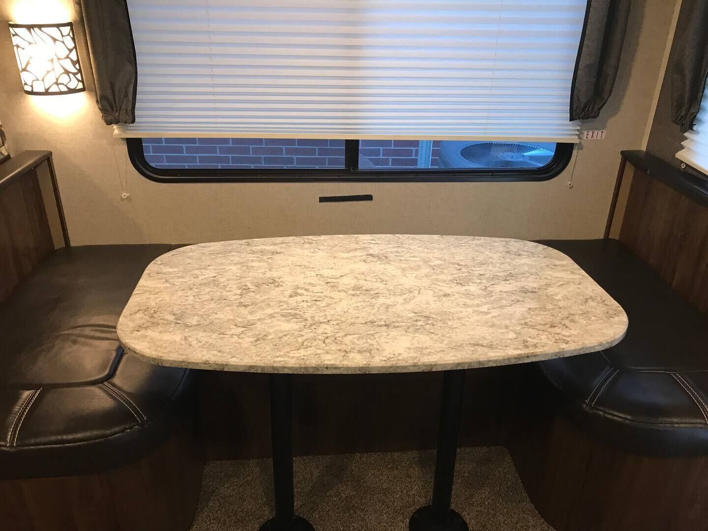 Interior de una caravana compacta con una mesa de mármol, dos sillones de cuero, una ventana con persianas y una lámpara empotrada en la pared.