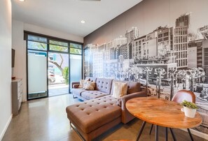 A modern living room with a large sofa, a round coffee table, and a cityscape mural on the wall. - 2 Modern Units in Heart of Little Italy! (San Diego)