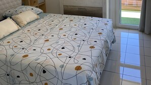 A bedroom with a bed, bedside tables, a mirror, a wall-mounted decoration, and a view of the outdoors. - Apartment in the heart of the wild south (Saint-Joseph)