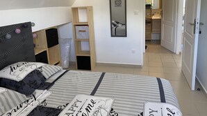 A bedroom with a bed, a wooden shelf, a mirror, and a door leading to a bathroom. - Apartment in the heart of the wild south (Saint-Joseph)