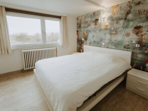 Ein Schlafzimmer mit einem großen Bett, einem Heizkörper, einem Fenster mit Vorhängen und einer Wand mit floralem Muster.