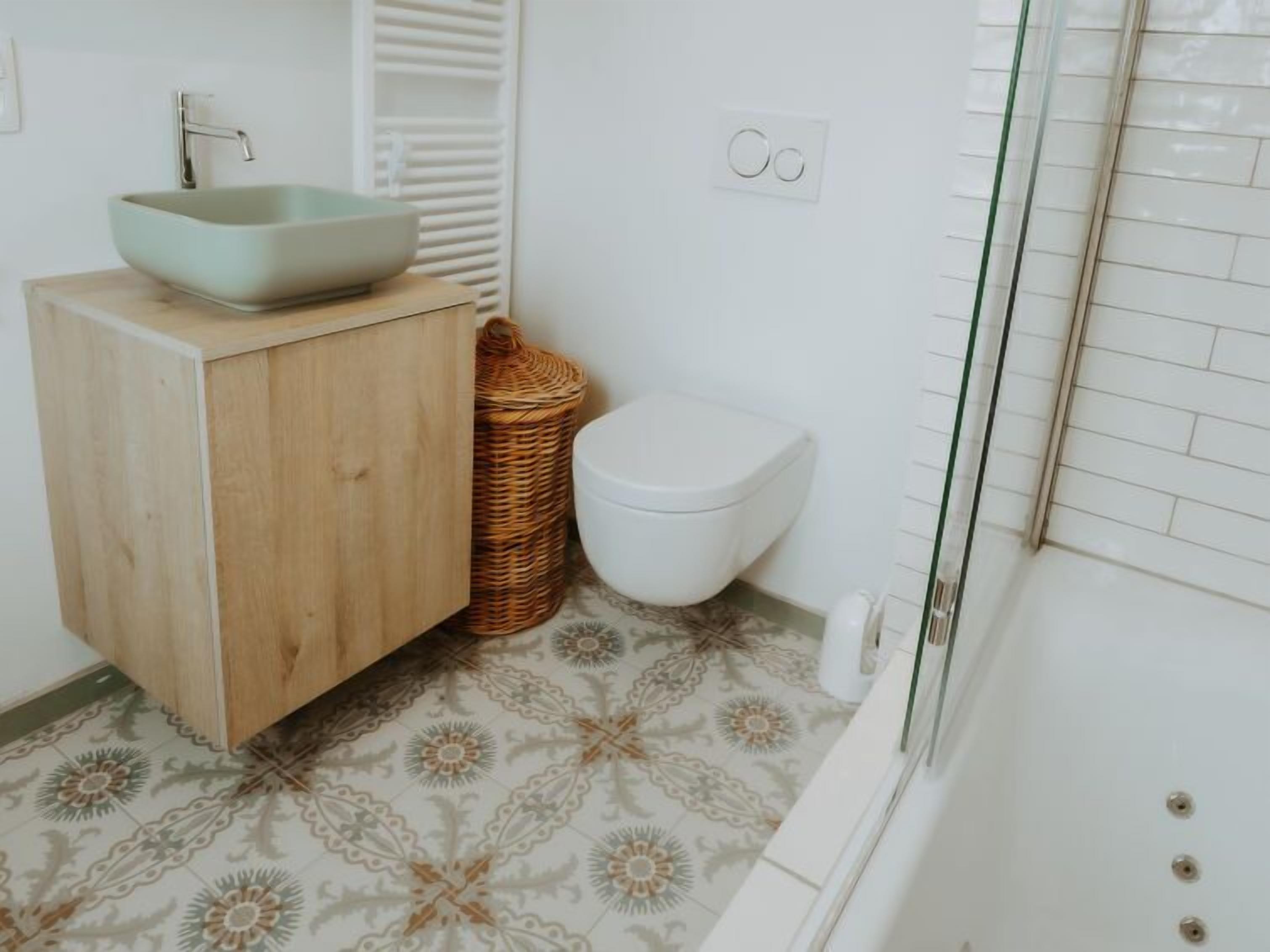 A bathroom with a wooden vanity, a white sink, a white toilet, and patterned floor tiles.