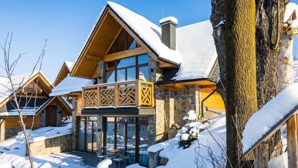 Un bâtiment de style chalet, avec une façade en bois, de grandes fenêtres et un balcon doté de balustrades en treillis.