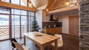 Un grand espace à manger avec une table et des chaises en bois, une cuisine équipée d’une cuisinière et de placards, et une grande fenêtre offrant une vue sur les montagnes.
