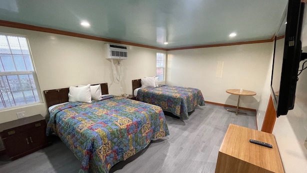 A hotel room with two beds, a small table, a TV, and an air conditioning unit. - Hilltop Motor Inn (Los Angeles)