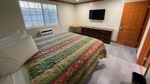 A bedroom with a bed, a dresser, a television, and a window. - Hilltop Motor Inn (Los Angeles)