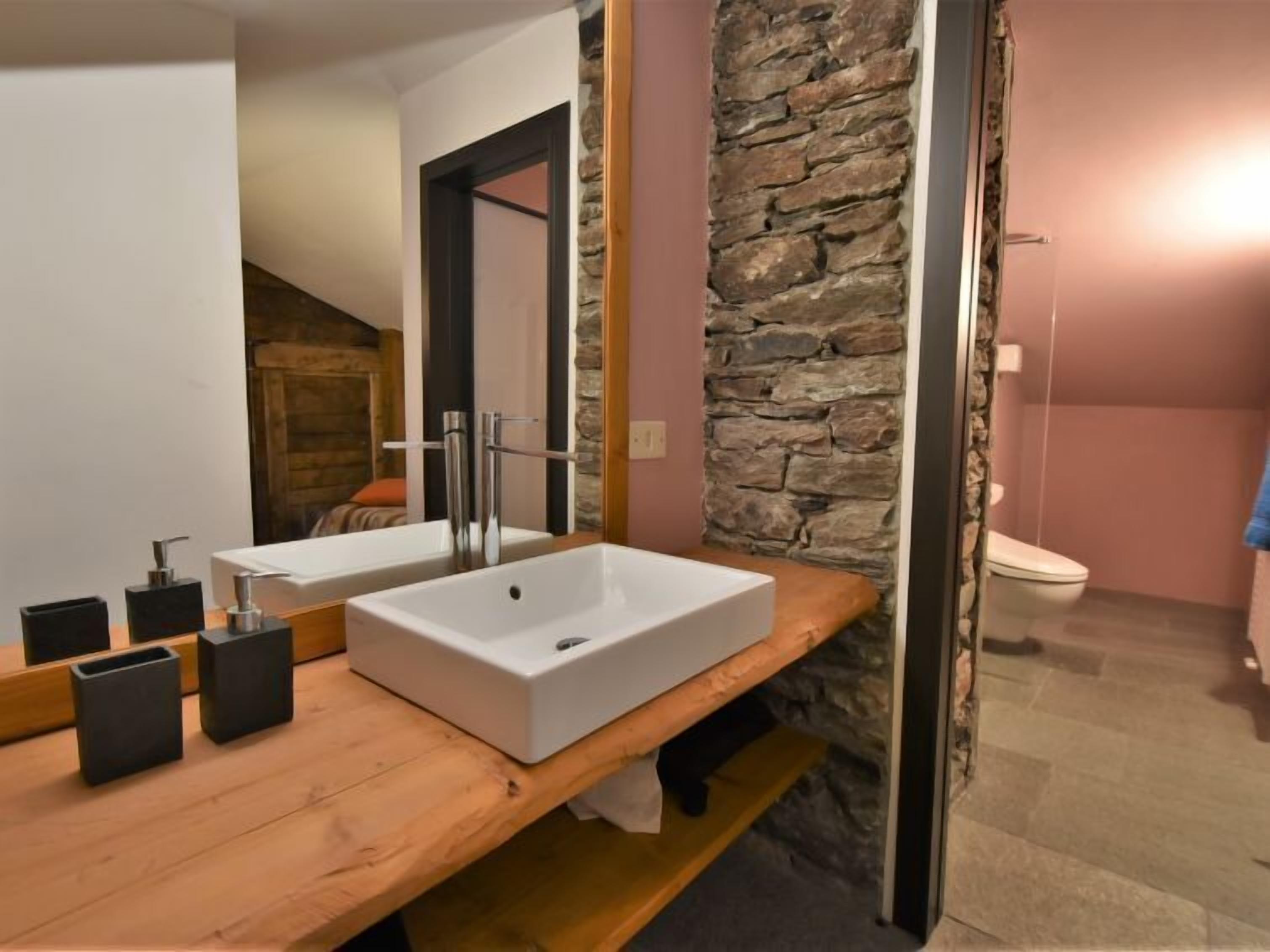 Ein Badezimmer mit einem Holzwaschtisch, einem weißen Waschbecken und einer Wand mit Steinakzenten.