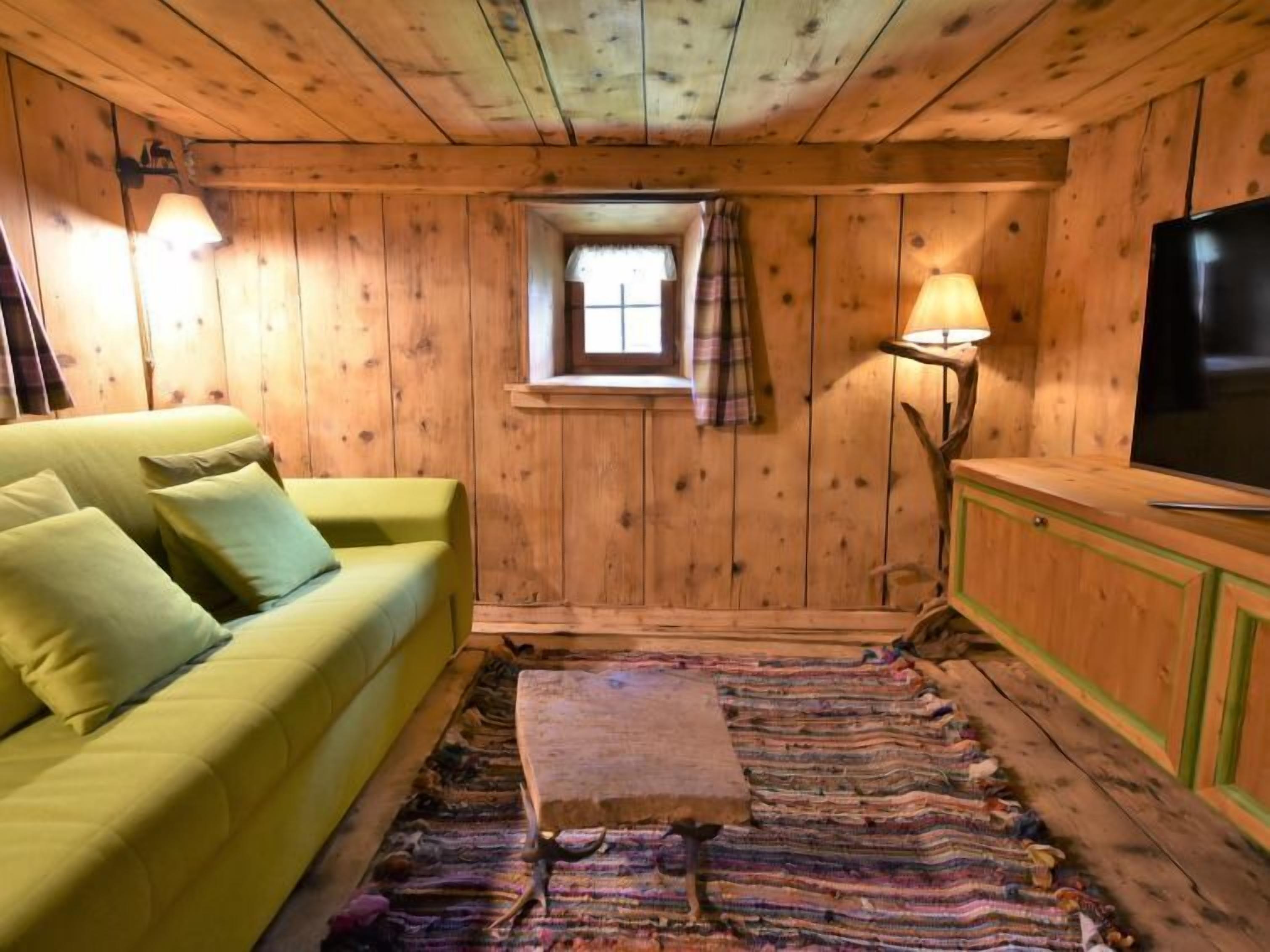 A cozy cabin room with a green sofa, a small window, a lamp, and a television.