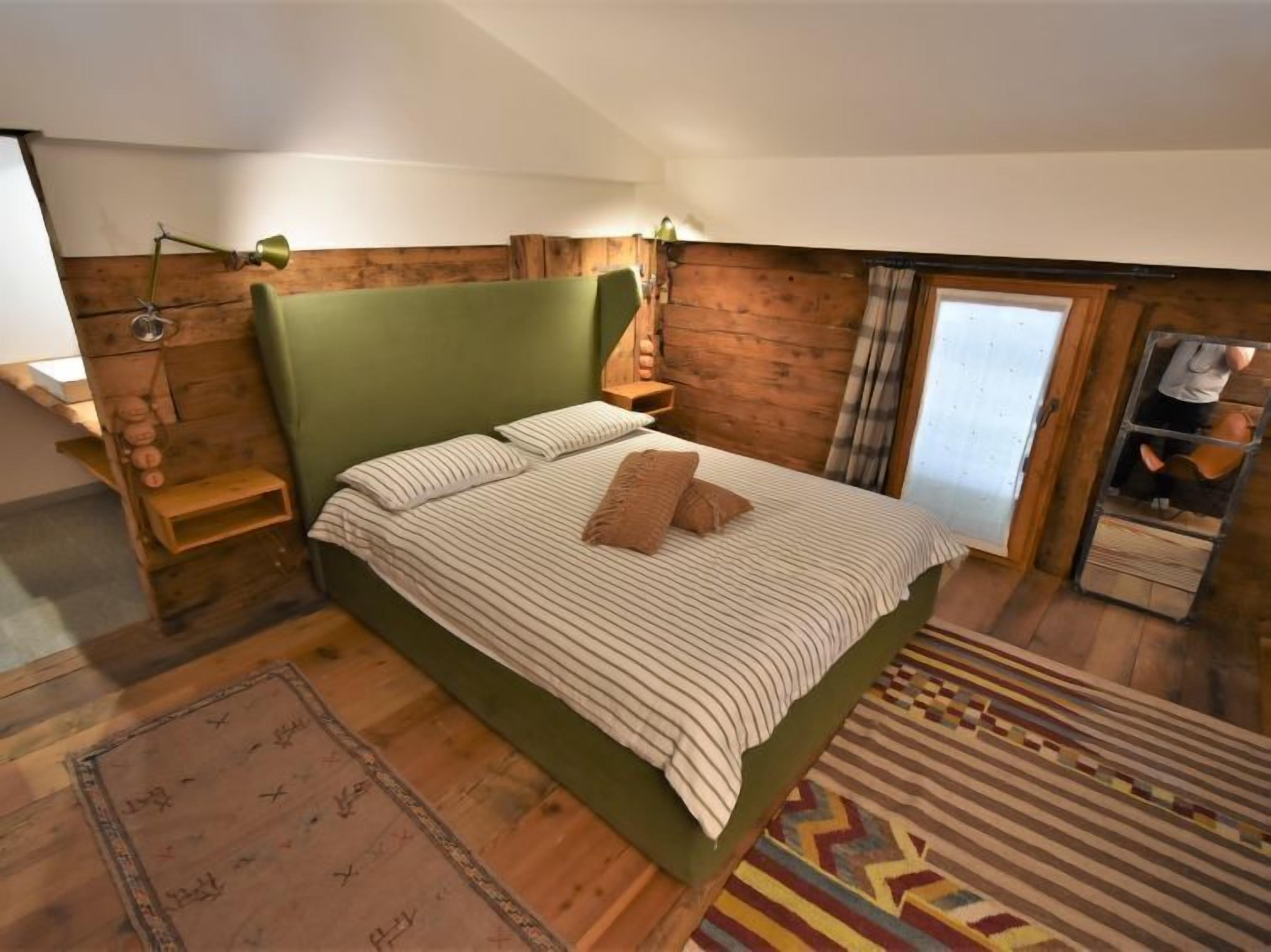 Ein gemütliches Schlafzimmer mit einem grünen Kopfteil, einer gestreiften Bettdecke und einem gemusterten Teppich.