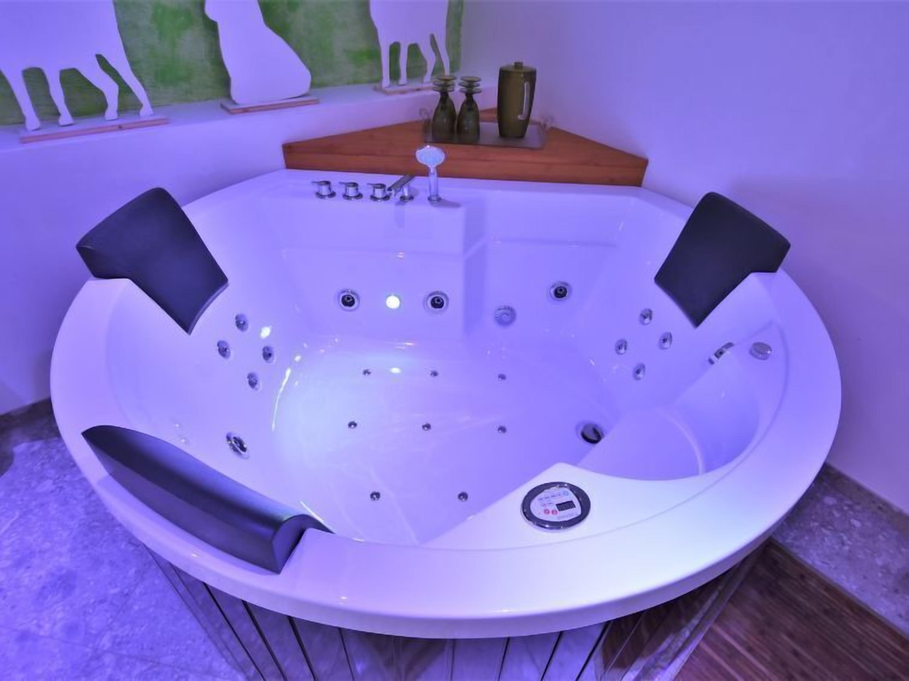 Een rond, wit bubbelbad met bedieningspaneel, omgeven door een houten terras en decoratieve muurdecoraties.