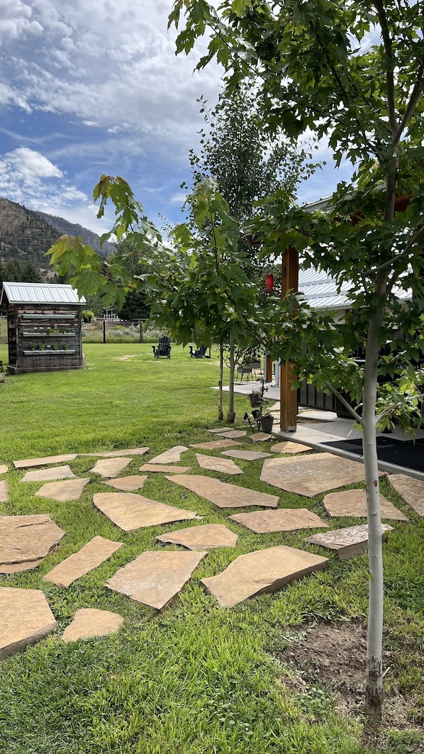 A stone pathway leading through a grassy area with trees and a wooden structure in the background.
