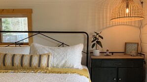 A bed with a metal frame, a bedside table with a plant, and a hanging light fixture.