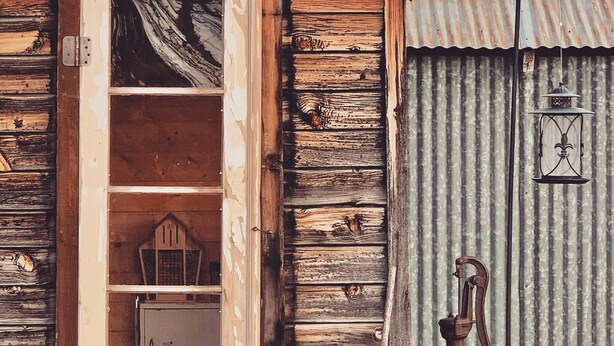 A rustic wooden building with a door leading to a storage area and a small porch area with a lantern.