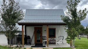 A single-story house with a metal roof, a front porch with chairs, and a gravel driveway.