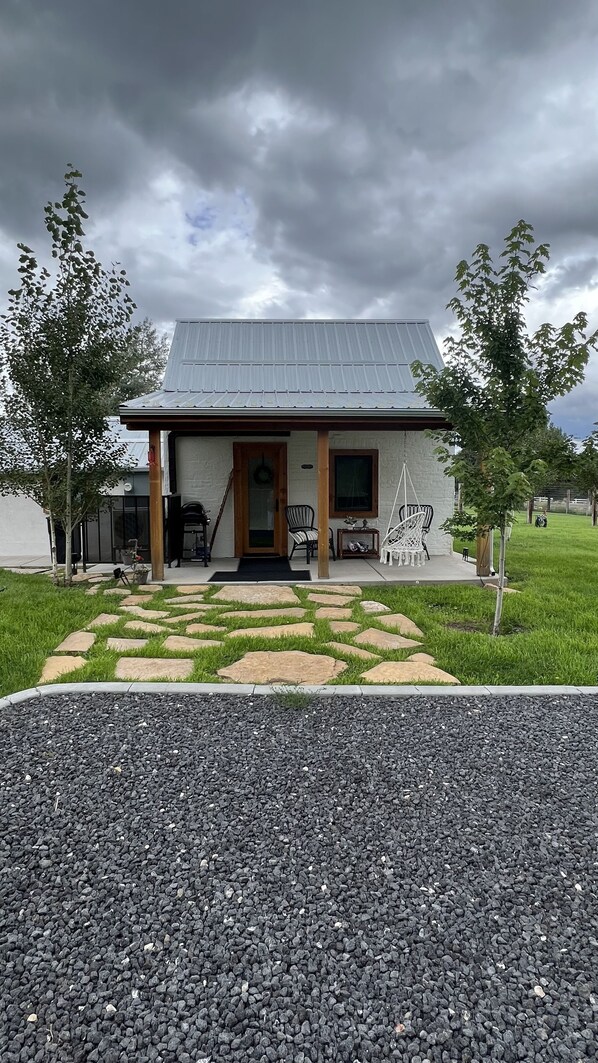 A single-story house with a metal roof, a front porch with chairs, and a gravel driveway.