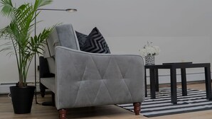 Una sala de estar moderna con un sofá gris, una planta en maceta, una lámpara de pie y un tapete blanco y negro.