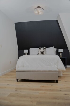 A bedroom with a large bed, a black accent wall, and a ceiling light fixture.