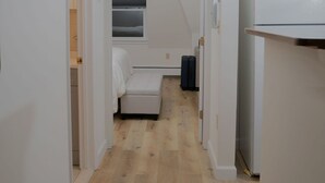 Un pasillo estrecho con piso de madera, un sofá blanco y una lámpara en el techo.