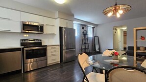 A modern kitchen with stainless steel appliances, a dining area with a glass table, and a wooden bookshelf. - A Modern and Executive Unit~1 Parking Spot&Great Location - Close To Everything (London)