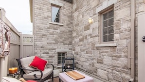 A stone-walled patio with outdoor seating, including a cushioned chair and a small table with a cutting board. - A Modern and Executive Unit~1 Parking Spot&Great Location - Close To Everything (London)