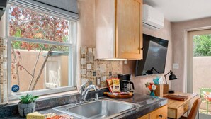 A modern kitchen with a large window, a sink, a stove, and a dining area with a table and chairs. - Studio Near Santa Fe Farmers Market (Santa Fe)