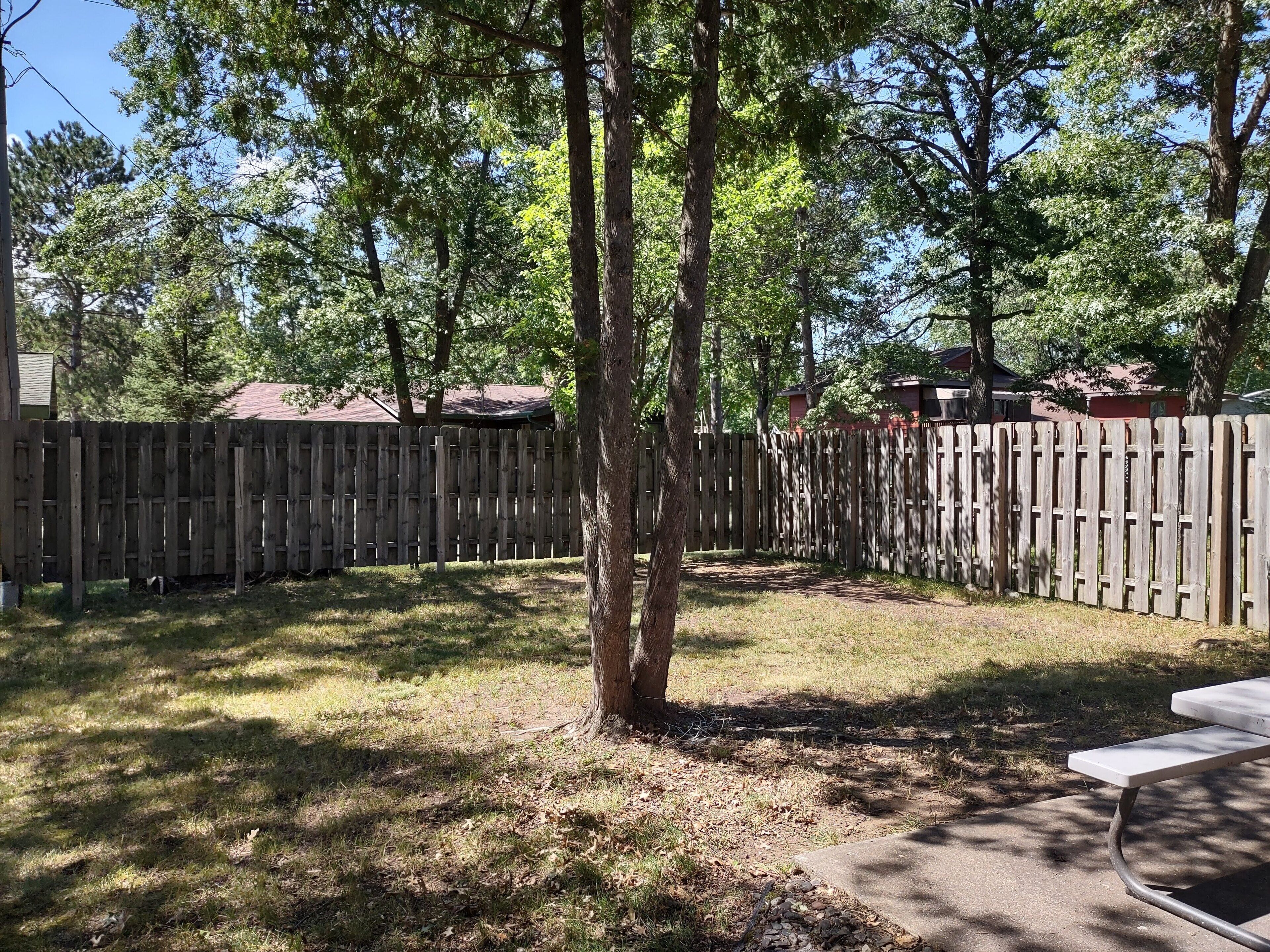 A backyard with a wooden fence, a tree, and a concrete patio area.