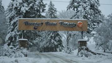 Un cartel de Breezy Point Resort con un logotipo, rodeado de árboles cubiertos de nieve.
