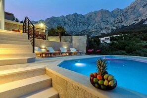 A pool area with steps leading up to a terrace, lounge chairs, and a fruit basket. - Villa Vivace with pool (Makarska)