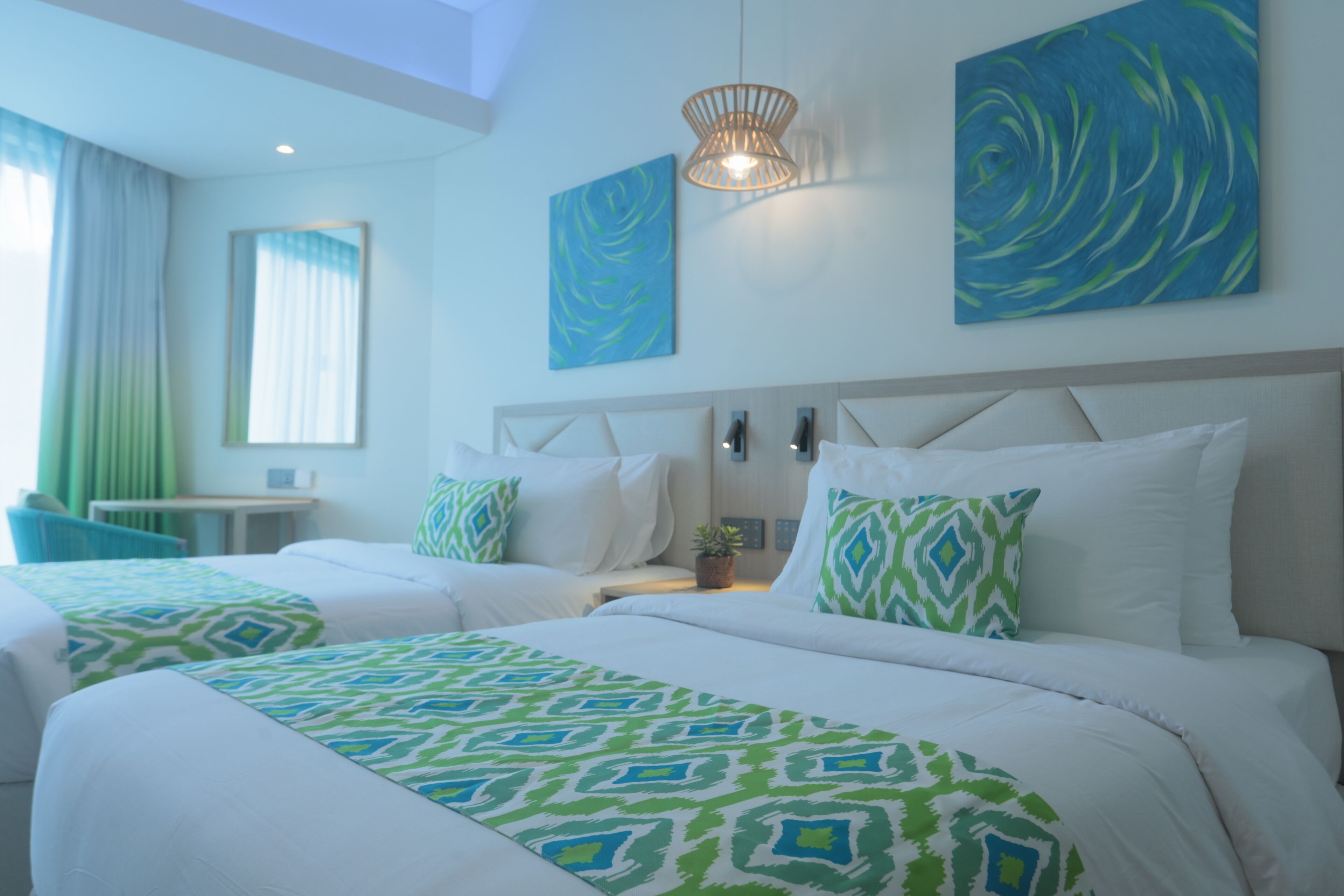 A hotel room with two beds, a large window with curtains, a wall-mounted lamp, and abstract art on the wall.